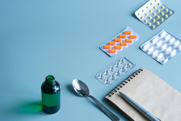 Open green vial with a medicinal potion next to a teaspoon, blister pills and vitamins. Treatment...