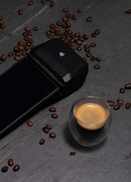 A Smart POS surrounded with coffee beans on black background. A shoot of espresso ready to be drink . Pay contactless NFC and enjoy the best coffee.