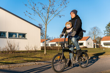 A father with little son in baby-carrier, sling is riding a bicycle outdoors, having a lot of fun....