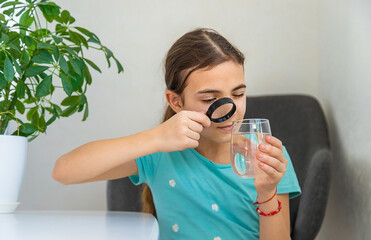 The child examines the water under a magnifying glass. Selective focus.