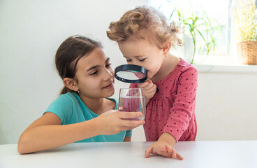 The child examines the water under a magnifying glass. Selective focus.