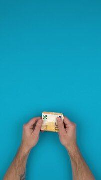 Vid&eacute;o verticale d'une personne qui manipule des billets de banque en euros, bras nus sur un fond bleu