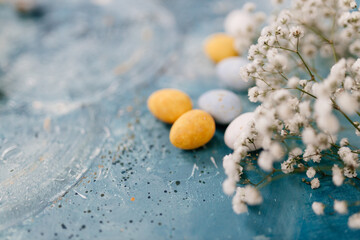 Blue, yellow, white eggs and white small flowers lie on a beautiful blue and turquoise picturesque background. Spring Background for Easter