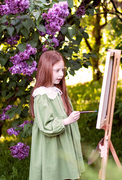 girl with long red hair draws in a lilac garden
