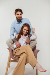 Happiness fashion couple. Smiling pretty redhead woman and brutal hipster handsome man sits on armchair and having fun on a white background