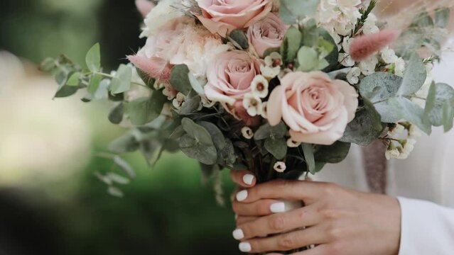 Close up of a bride holding flowers in garden. Charming woman holds wedding bouquet of flowers outdoors