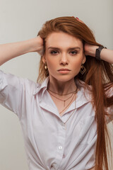 Fototapeta premium Fashion fresh redhead beauty woman with cute face in fashionable white shirt fixes long red hair on a white background