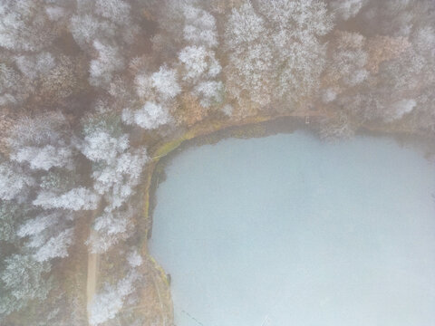 Aerial view or top view of winter forest lake, showing the ice on the lake and the pine trees with snow covered. Winter background shot by a drone. High quality photo
