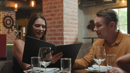 Medium shot of cheerful family couple smiling and discussing dishes in menu while having dinner in restaurant - Powered by Adobe