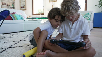 Two small boys playing video game on screen. Brother holding tablet with joystick plays with console