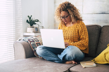 One adult modern woman at home working on laptop alone sitting on the sofa inside apartment, Indoor technology leisure activity female people surfing the net on notebook computer. Smart working relax - Powered by Adobe