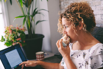 Woman eating sandwich and working on laptop at the same time. Modern fast food and smart working home people technology activity. Businesswoman using computer to surf the net alone indoor leisure