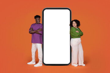 Positive mixed race couple standing by big cell phone, mockup