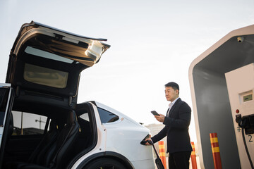 Smiling asian businessman looking at smartphone screen while plugging in charging cable into...