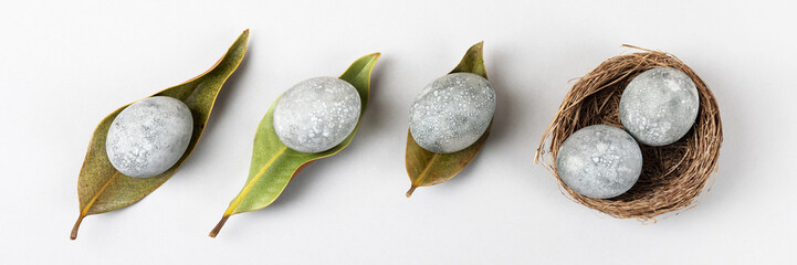 Minimal ecological Easter concept with dried flowers. Gray eggs on dry magnolia leaves and in a...