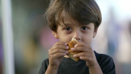 Portrait of child eating piece of bread croissant. Close up face of one small boy kid eating carb food