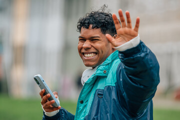 Fototapeta premium young latino man smiling with mobile phone in the street waving