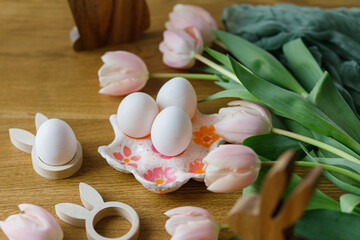 Beautiful tulips, natural eggs and bunny decoration on rustic wooden table. Happy Easter! Modern farmhouse easter decor. Stylish handmade egg holder, pink tulips and wooden bunny