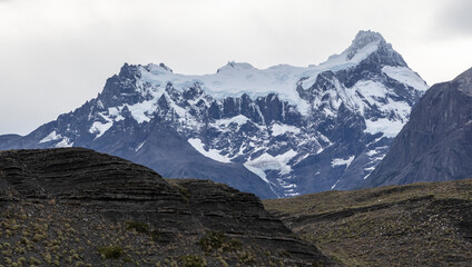 Snowy mountains behind grassy hills of Torres del Paine National Park in Chile, Patagonia, South America