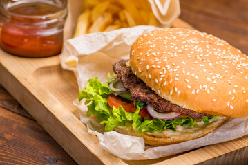 Burger with cutlet in a white bun on the background of french fries and tomato sauce