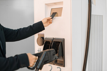 Close up of stylish asian entrepreneur taking power cord at charging station and paying with credit card for energy. Wireless technology in city infrastructure.
