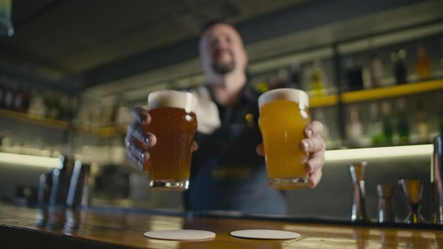 The bartender puts two glasses of beer on the bar counter. Fun evening in the pub with ale and lager. High quality 4k footage