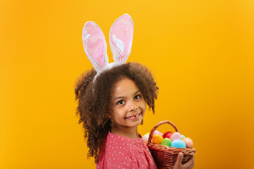 Obraz na płótnie Canvas A Black girl with rabbit ears on her head with a basket full of colored eggs.