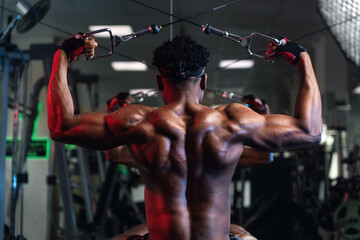 20s Black male working out rear delt and back muscles with cable machine