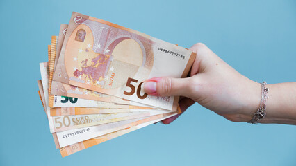 Woman's hand holding fifty euro banknotes on a blue background.
