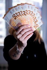 Woman holding a bunch of 50 euro banknotes in her hand.