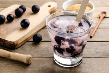 Brazilian jabuticaba caipirinha in a glass with ice and fruits over wooden table