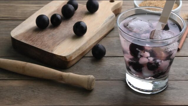 Brazilian jabuticaba caipirinha in a glass with ice and fruits over wooden table.