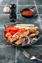 Grilled chicken skewers with vegetables and tomato sauce on black tile background.