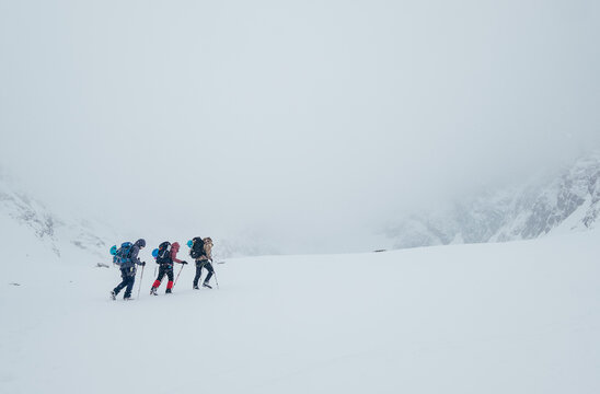 Three members rope team ascending the high mountain winter peak. Blizard covering the structural basin in Vysoke Tatry (High Tatras) mountains under Lomnicky Stit roky mountain. Extreme sport concept.