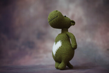 
a small knitted dark green hippopotamus with a white heart on its chest stands on a beautiful background