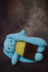 a blue knitted rabbit with big ears in a yellow vest and brown pants in a photo studio on a beautiful background