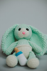 cute knitted light green bunny with big ears in a white diaper with a knitted white pacifier with two skeins of white and light green knitting yarn