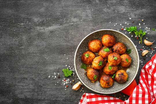 Meatballs in tomato sauce with herbs at dark table. Flat lay image with space for text.