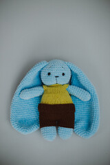 a blue knitted rabbit with big ears in a yellow vest and brown pants