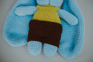 a blue knitted rabbit with big ears in a yellow vest and brown pants