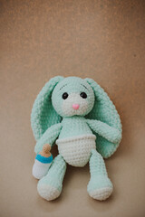 cute knitted light green bunny with big ears in a white diaper with a knitted white pacifier