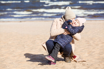 Mother hugs and kisses her three-year-old daughter, walking along the sandy beach,copy space