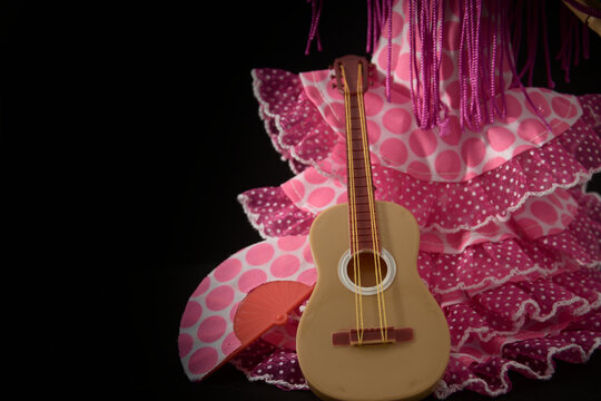 Flamenco woman's dress or faralaes, a guitar and a fan on black background with copy space