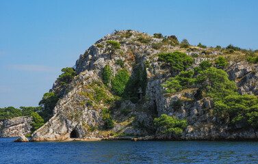 Fototapeta na wymiar A small cave in a limestone rock covered with pine trees in the Adriatic Sea, Croatia.