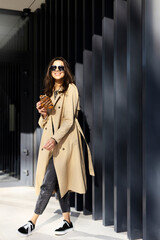 Naklejka premium Young, beautiful woman in a beach coat holds a fresh croissant in her hand. A girl in sunglasses on the street.