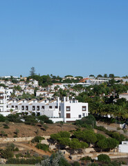 Fototapeta na wymiar Holiday houses of white colour in the summer resort in Algarve, Portugal. Panoramic view from far. Verical photo
