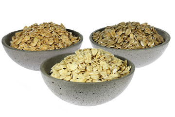 cereal flakes (spelt, oat, rye) in concrete bowls isolated on white background