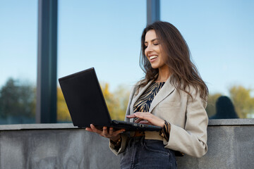 Beautiful, smiling girl copywriter works on a laptop on the street. Work online, work on the...