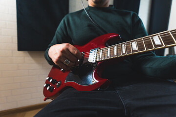 Obraz premium young musician man playing the red bass guiatar at home, closeup. High quality photo