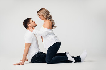 a blonde pregnant woman with a man sitting on the floor in a white room. 